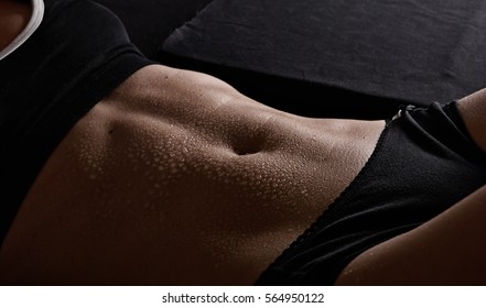 Young woman training abs.  Black background. Close-up