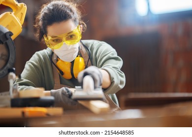 Young woman is training to be a carpenter in workshop.
