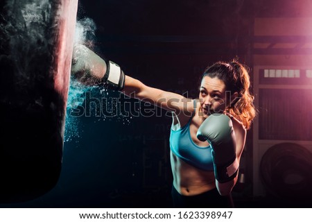young woman training boxing in the punching bag - sport, self defense, boxing and training concepts - swing boxing