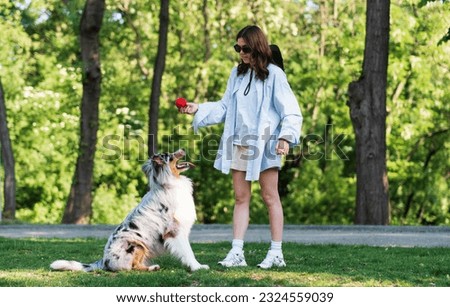 Young woman training her aussie shepherd dog in green park. Active lifestyle for an australian collie, playing fetch on the lawn