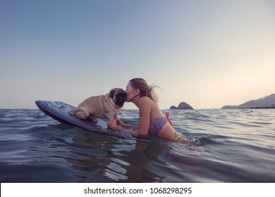 Young woman training her dog to stand up paddle in the sea, girl having fun with her pet on the beach