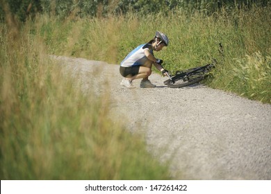 Young Woman Training On Mountain Bike And Repairing Flat Tyre On Track In Countryside