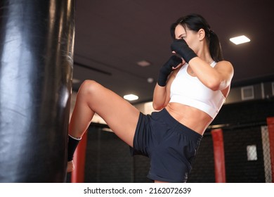 Young woman trains in kickboxing ring with heavy punching bag. Foot kicks or knee Strike