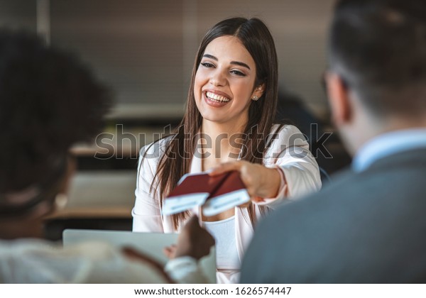 Young woman travel agent with flight tickets in hands.\
Travel agent giving tickets and passport to tourist. Young couple\
in a tour agency communication with a travel agent travelling\
concept 