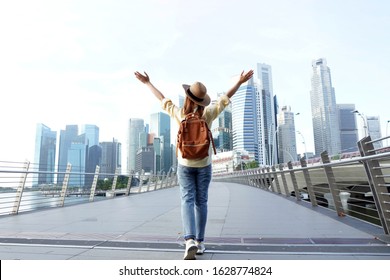  Young woman traveler with backpack and hat traveling into Singapore city downtown. Travelling in Singapore concept.                                     