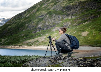 Young woman traveler professional photographer takes a picture of the landscape on the camera on a tripod, Norway, beautiful northern nature