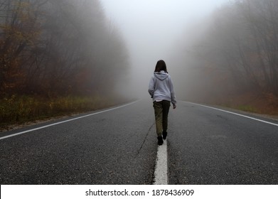 Young Woman Traveler, Rear View On Foggy Road In Autumn Forest