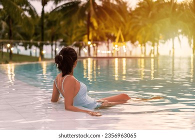 Young woman traveler relaxing and enjoying the sunset by a tropical resort beachfront pool while traveling for summer vacation