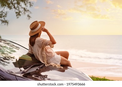 Young Woman Traveler Sitting On A Car And Looking A Beautiful Sunset At The Beach While Travel Driving Road Trip On Vacation