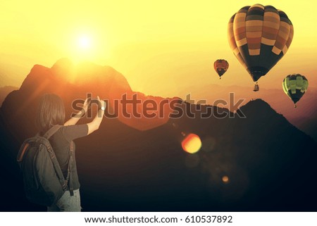 Young woman traveler taking photo of mountains with hot air balloons in sunset. Life and lifestyle concept.Vacation and long weekend. Dawn in mountains with sun flare.
