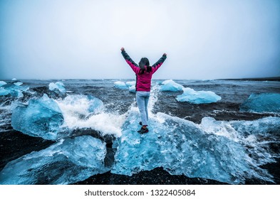 Young Woman Traveler Travel To Diamond Beach In Iceland. Frozen Ice On Black Sand Beach Known Flows From Jokulsarlon Beautiful Glacial Lagoon In Vatnajokull National Park, Southeast Iceland, Europe.