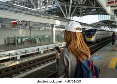 Young woman traveler using travel app in smart phone for checking timetable at train station