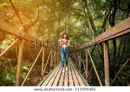 young woman traveler walking on the bridge with backpack and tablet in amazing forest, wanderlust travel concept