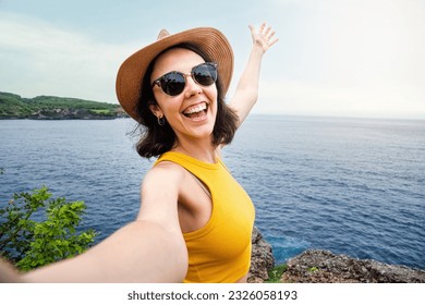 Young woman traveler wearing hat and sunglasses taking selfie in Nusa Penida, Bali. Female taking picture in vacation. - Powered by Shutterstock