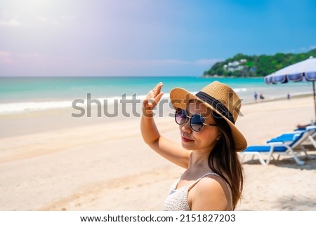 Young woman traveler wearing sunglasses covering face by hand to protect UV rays from the sun at tropical sandy beach on sunny day, Skin care and eyes protect concept
