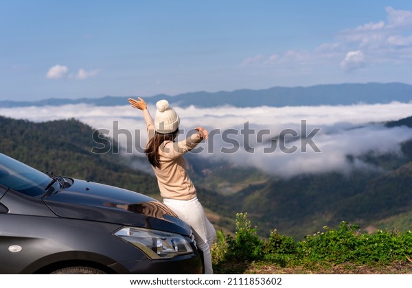 Young\
woman travelers with car watching a beautiful sea of fog over the\
mountain while travel driving road trip on\
vacation
