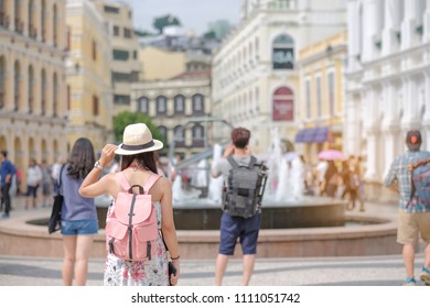 Young Woman Traveling Backpacker With Hat, Asian Traveler Standing On Senado Square, Landmark And Popular For Tourist Attractions In Macau. Travel Concept