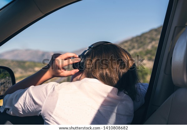 \
Young woman traveling by\
car listen music in the headphones and looks out the open window of\
the auto