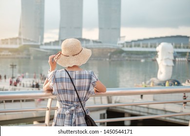 Young Woman Traveling With Hat In The Morning, Happy Asian Traveler Visit In Singapore City Downtown. Landmark And Popular For Tourist Attractions. Asia Travel Concept