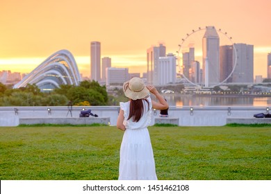 Young Woman traveling with hat at Sunset, happy Asian traveler visit in Singapore city downtown. landmark and popular for tourist attractions. Asia Travel concept