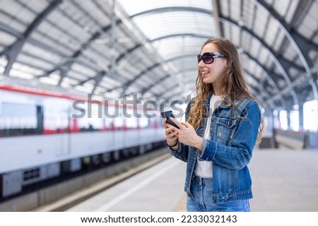 Young woman traveling, sitting in the train looking out window. Enjoying travel. Caucasian traveler woman traveling by Mass Rapid Transit(MRT) train using smartphone. Transportation, travel concept.
