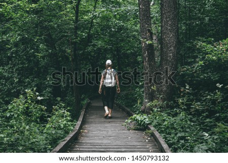 Young woman traveller with backpack on wooden pathway or walkway from wood planks in forest park, toned