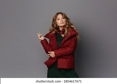 Young woman in trendy red winter coat posing at the grey background, studio shot