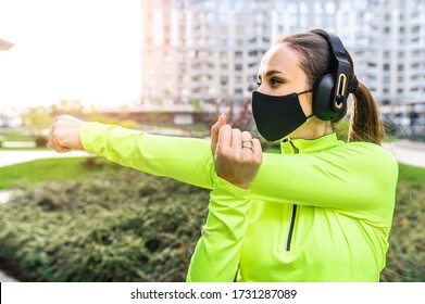 A Young Woman In Trendy Sportswear With A Black Medical Mask On The Face Is Doing Warming Up Before Workout Outdoors. Sports Training During Quarantine