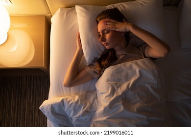 Young woman tries to fall asleep tossing and turning in bed at night. Sleepless lady lies in hotel room with switched on lamp upper close view - Shutterstock ID 2199016011