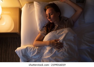 Young woman tries to fall asleep tossing and turning in bed at night. Sleepless lady lies in hotel room with switched on lamp upper close view - Shutterstock ID 2199016019