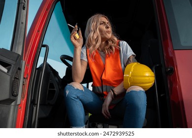 Young woman truck driver with hard hat smoking cigarette with open door of the truck. She had enough, bad day - Powered by Shutterstock