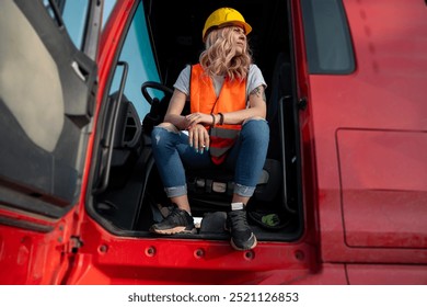 Young woman truck driver with safety vest and hard hat sitting on the drivers seat with doors open, resting  - Powered by Shutterstock