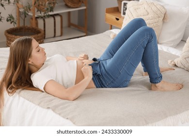 Young woman trying to button tight jeans in bedroom. Weight gain concept - Powered by Shutterstock