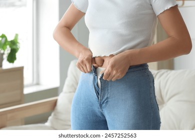 Young woman trying to button tight pants at home, closeup. Diet concept - Powered by Shutterstock