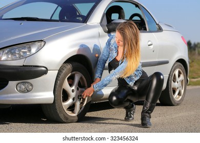 young woman trying to change wheel on the road