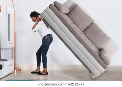 Young Woman Trying To Move Large Sofa At Home