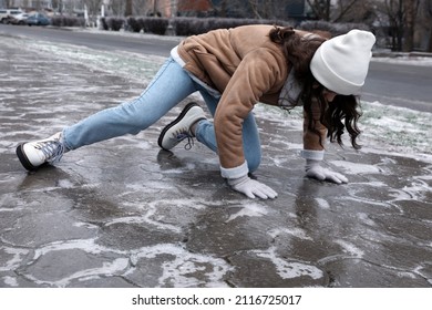 Young woman trying to stand up after falling on slippery icy pavement outdoors