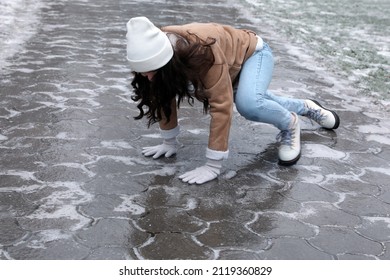 Young Woman Trying To Stand Up After Falling On Slippery Icy Pavement Outdoors