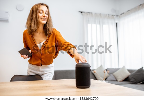 Young woman turning on wireless smart column at\
home. Concept of a smart home wireless devices. Concept of smart\
home and voice command\
control