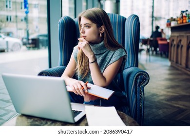 Young Woman In Turquoise Sweater And Ripped Jeans Thoughtfully Looking Out Window While Sitting At Cafe And Making Up Interview Questions