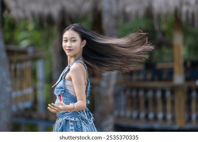 A young woman twirls gracefully, her long hair flowing behind her, wearing a stylish denim outfit in a natural outdoor setting. - Powered by Shutterstock