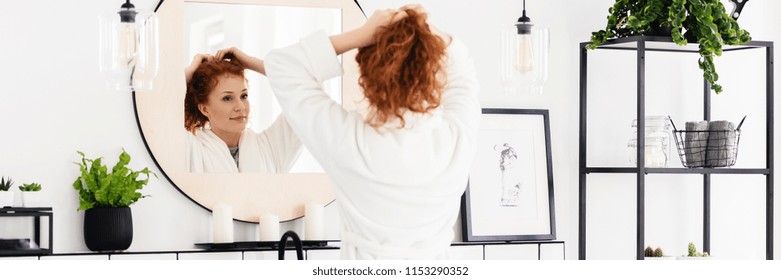 Young woman tying up her hair in bright bathroom interior with black furniture, modern lamps and fresh plants - Powered by Shutterstock