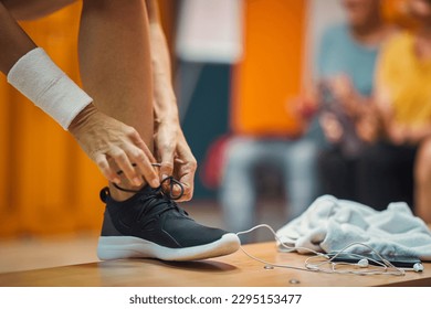 Young woman tying her shoe in gym locker room, with earphones and towel on bench, getting ready for workout. Helath, lifestyle, active concept. - Powered by Shutterstock