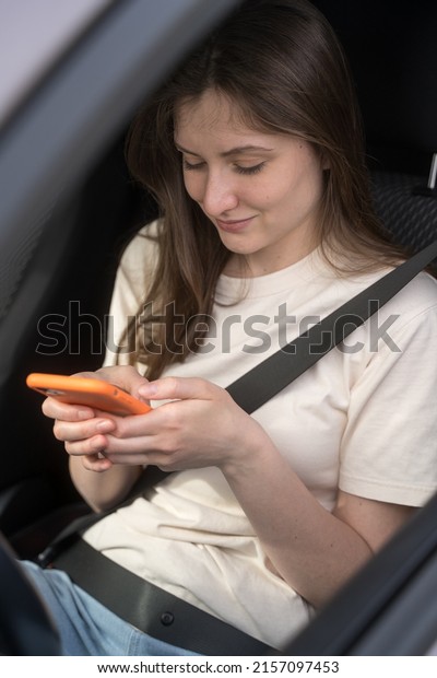 Young woman types in the\
messenger behind the wheel of a car. Using a mobile phone in\
automobile