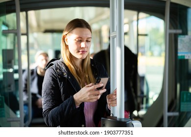 Young woman typing messages on phone on way to work in modern streetcar on sunny autumn day