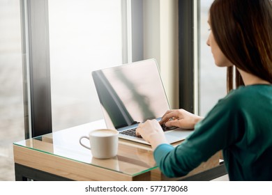 Young Woman Typing On Computer In Front Of The Window