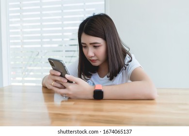 Young woman typing text message on smart phone in cafe. Asian girl wearing smart watch hand holding cellphone reading incoming sms message notification connected free wifi in coffee shop table.