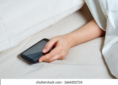 Young Woman Under Duvet With Smart Phone. Girl Sleeping In Bed And Holding A Cell Phone. Phone Addiction.