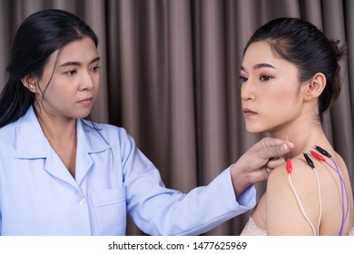 young woman undergoing acupuncture treatment with electrical stimulator on shoulder with doctor