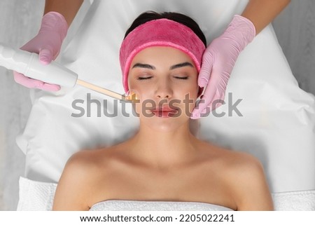 Young woman undergoing face rejuvenation procedure with darsonval in salon, top view